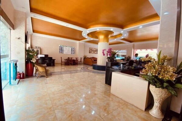 A lobby with a marble floor, a reception desk, a seating area, and a large decorative column.