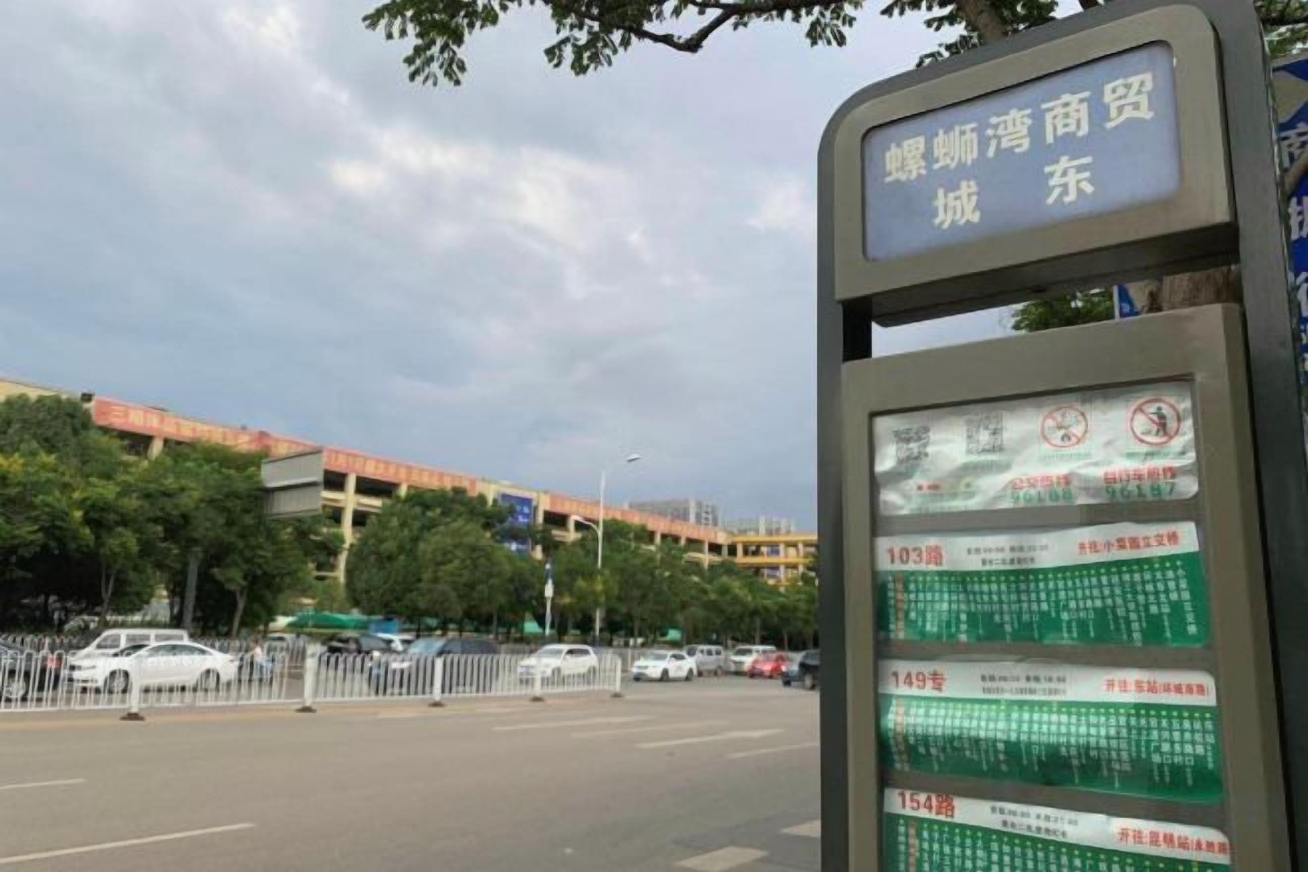 A bus stop with a digital display board and a building in the background.