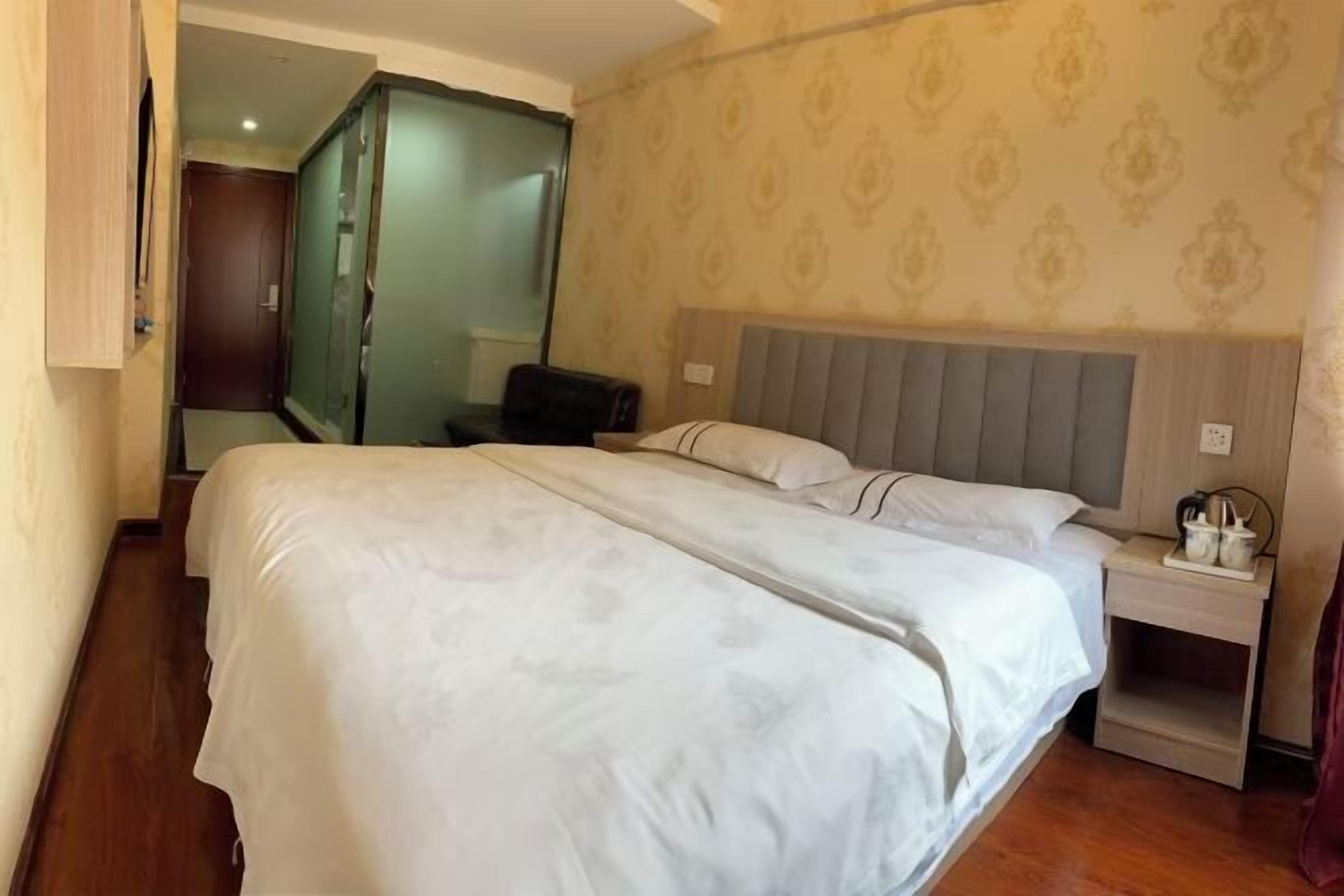 Hotellihuone, jossa on suuri sänky, yöpöytä lampun kanssa ja vaatekaappi.