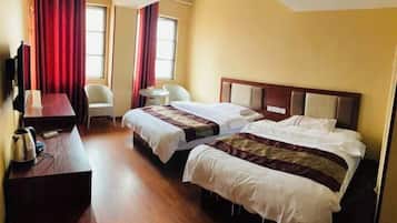 A hotel room with two beds, a desk, a chair, and a TV.