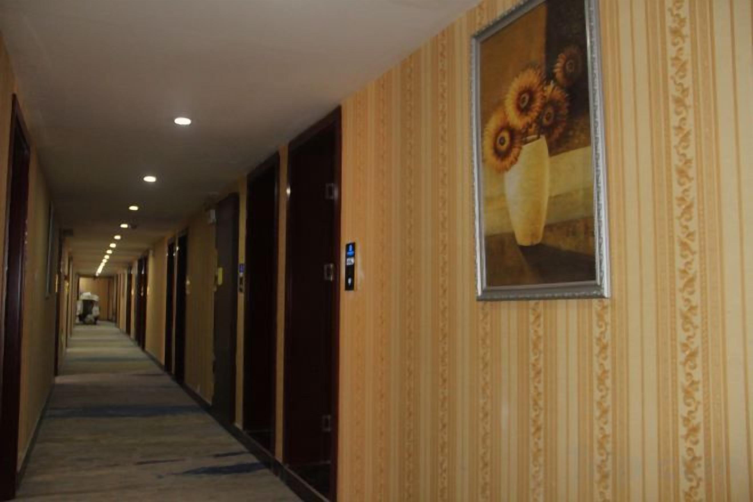 Een hotelgang met deuren links, een vloerbedekte vloer en een lijst met een afbeelding aan de rechterwand.