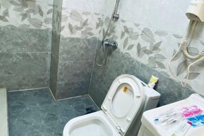 Un baño con inodoro, ducha y secador de pelo en la pared.