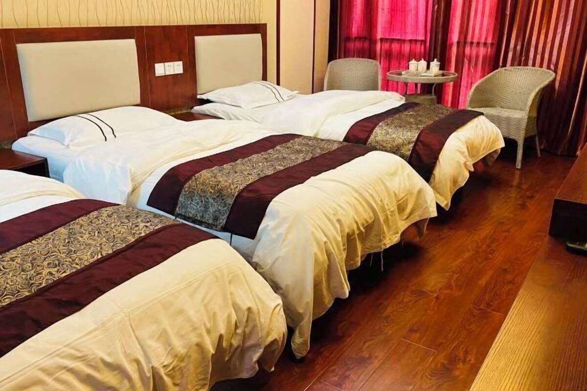 Ein Hotelzimmer mit drei Betten, einem kleinen runden Tisch mit einem Stuhl und Holzboden.