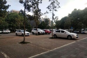 A parking area with several cars, trees, and buildings in the background.