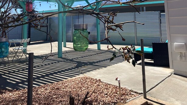 Eine Terrasse mit einer Pergola, einer grünen Glasflasche und einem Metallstuhl.