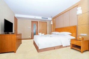 A hotel room with a bed, a wooden nightstand, a TV on a dresser, and a wooden wardrobe.