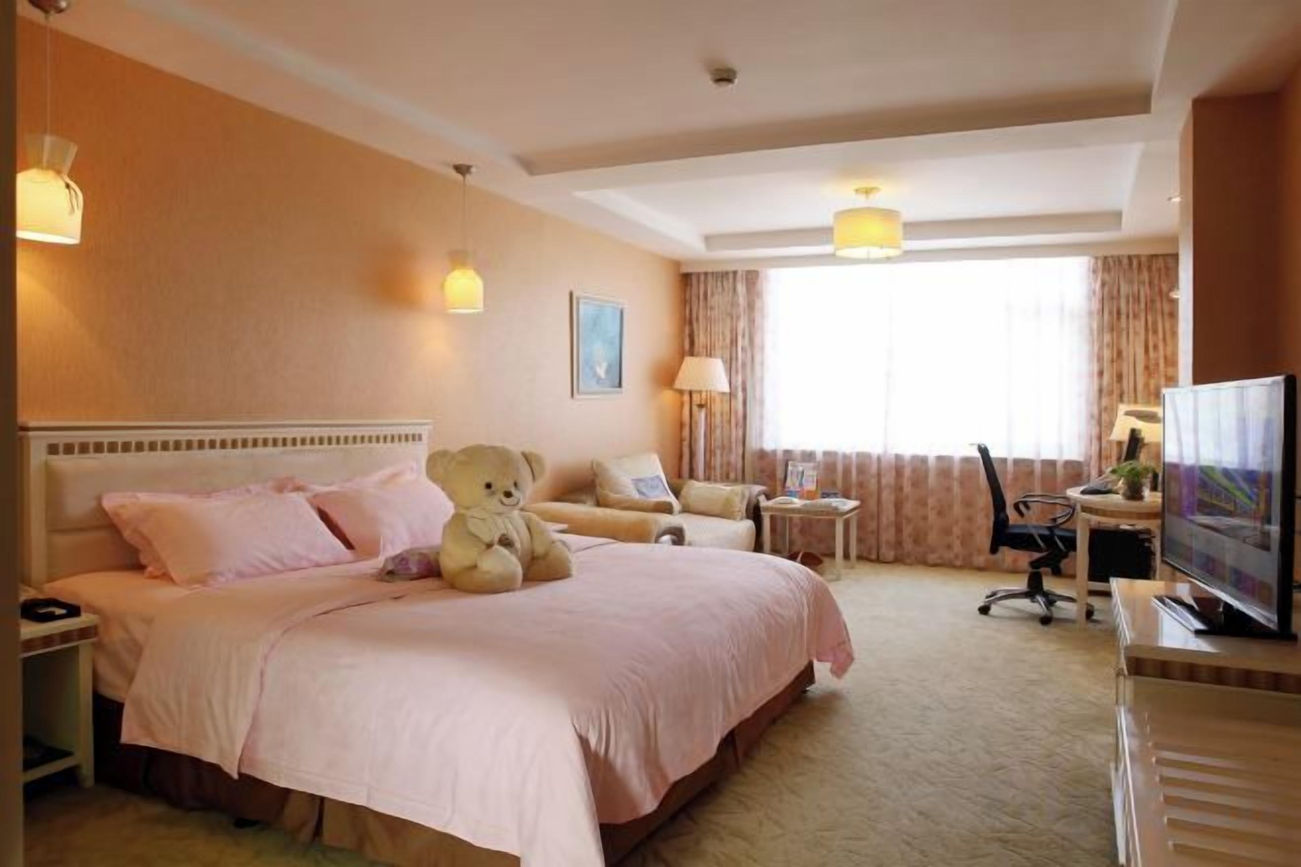 A hotel room with a large bed, a desk, a chair, a television, and a window with curtains.