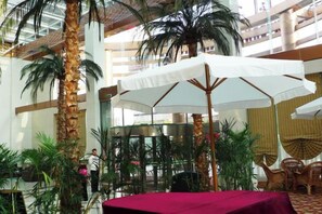 An indoor atrium with a red table, white umbrellas, and palm trees. - Yuanli International Hotel (Suichang)