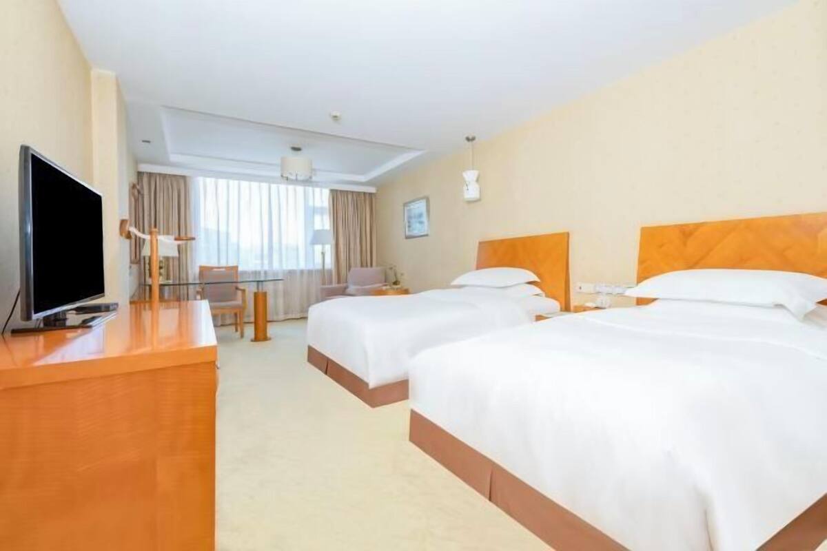 Habitació d'hotel amb dos llits, una taula de treball amb televisió, una cadira i una finestra amb cortines.
