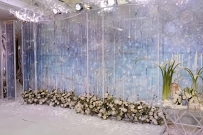 Une pièce avec un mur décoratif, un arrangement floral blanc et une petite table sur laquelle est posée une plante.