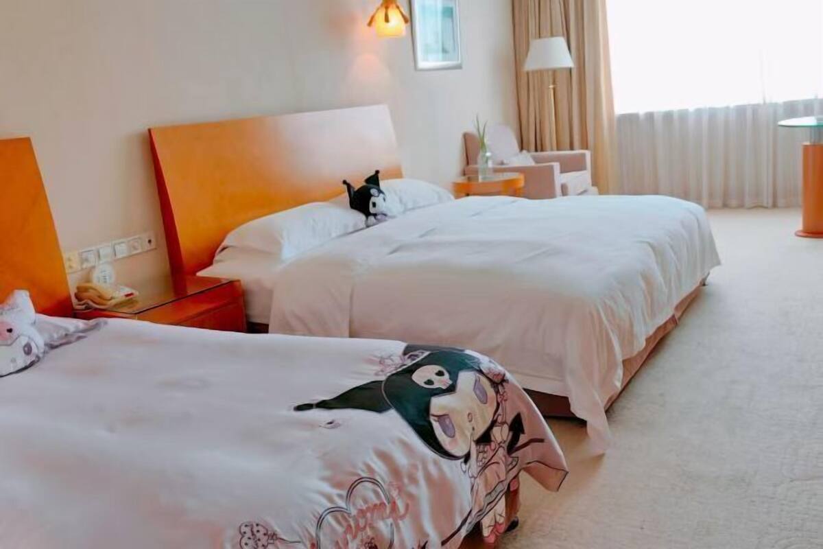 Habitació d'hotel amb dos llits, una tauleta de nit, una làmpada i una finestra amb cortines.