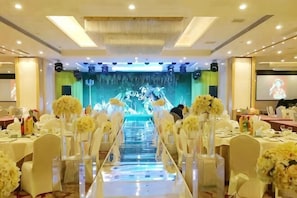 Une salle de banquet avec des rangées de tables, des chaises blanches et des centres de table ornés de compositions florales.
