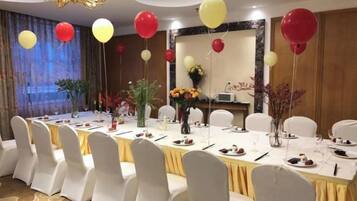 A banquet hall with a long table set for a formal event, surrounded by white chairs.
