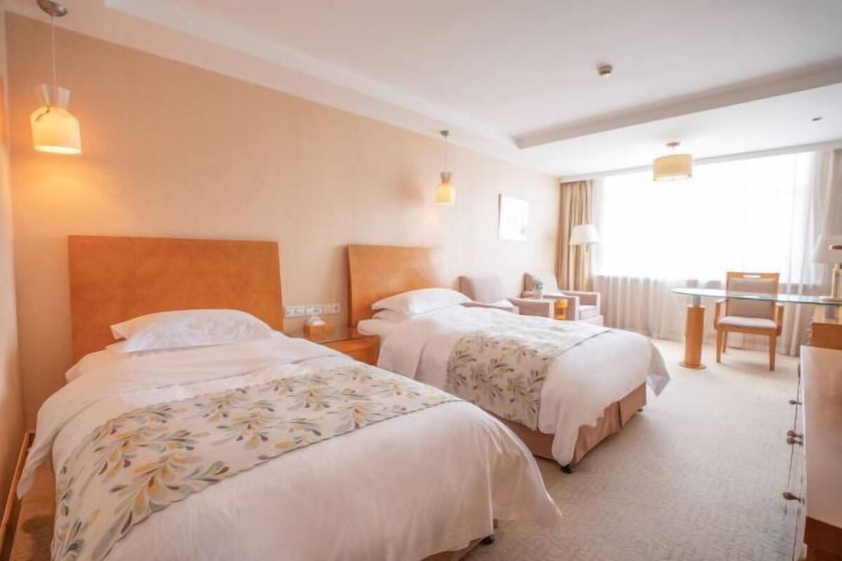 Una habitació d'hotel amb dos llits, una taula de treball, una cadira i una finestra amb cortines.