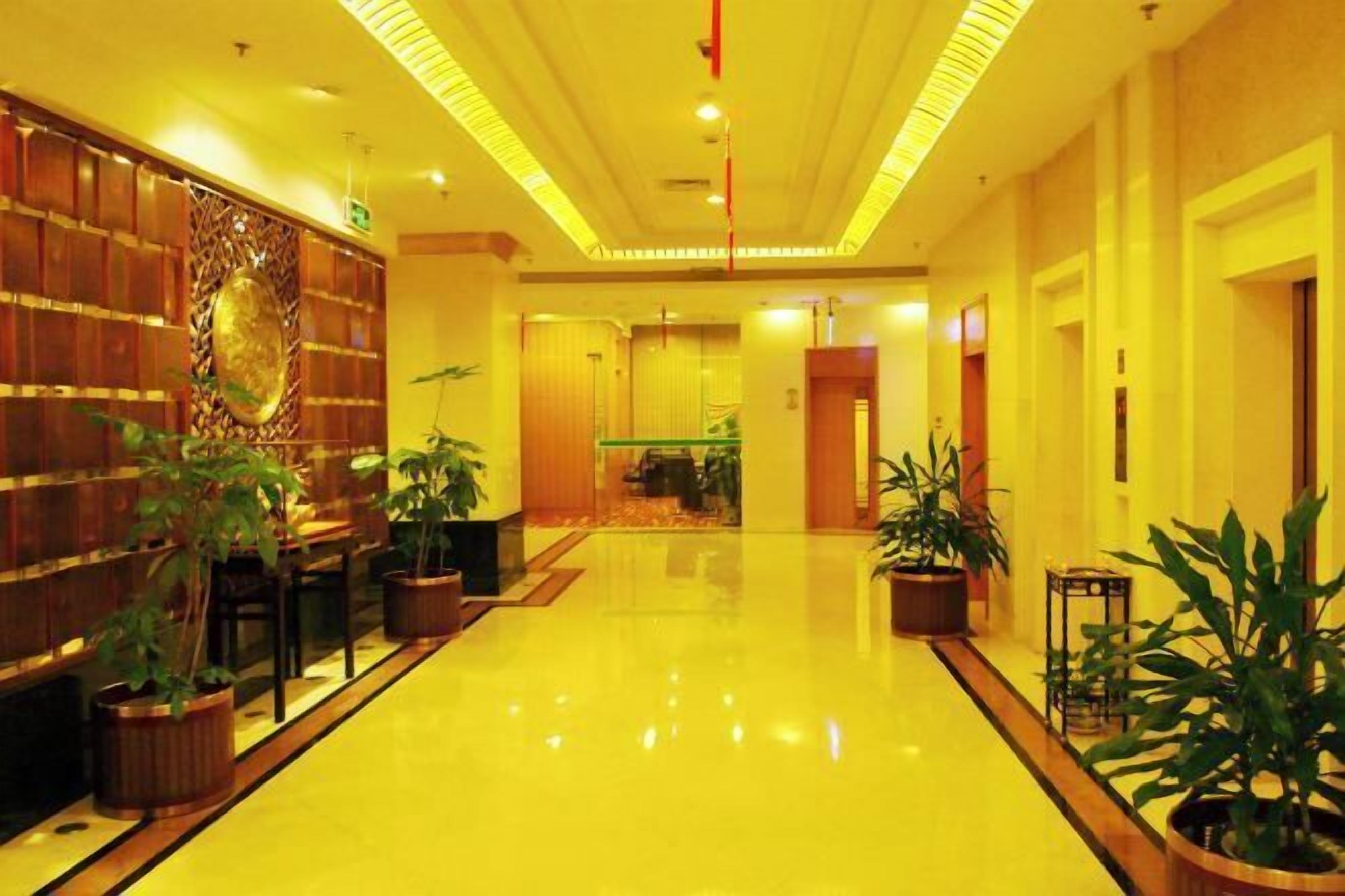 A hotel lobby with a polished floor, wooden paneling, and potted plants.