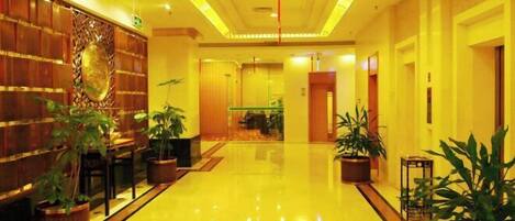 A hotel lobby with a polished floor, wooden paneling, and potted plants.