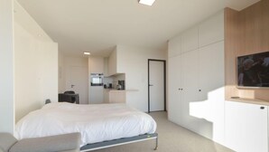 A modern hotel room with a large bed, a desk, a chair, a TV, and a kitchenette. - Astrid 802 with parking by Interhome (Bredene)