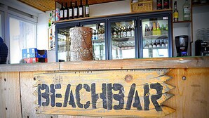 En træskranke med et skilt der siger "BEACHBAR" og en stor træstamme-pynt.