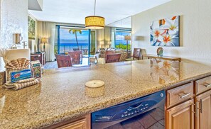A kitchen with granite countertops, a dishwasher, and a dining area with chairs and a table.