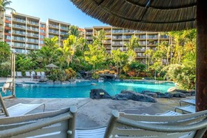 A resort with a pool surrounded by palm trees and a thatched roof structure.
