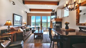 Ein geräumiges Wohnzimmer mit großem Fenster, Holzboden und einem Essbereich mit einer Kristallleuchtre.