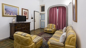 Una sala de estar con una televisión, dos sillones, un sofá, un tapete estampado y cuadros enmarcados en la pared.