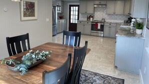 A modern kitchen with white cabinets, stainless steel appliances, and a dining area with a wooden table and chairs. - Charming newly-renovated historic log house near PSU and Spruce Creek (Tyrone)