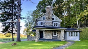 A two-story stone house with a stone chimney, a front porch, and a small attached garage. - Charming newly-renovated historic log house near PSU and Spruce Creek (Tyrone)