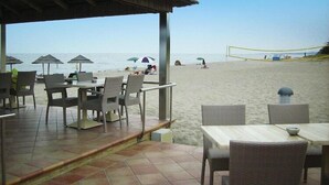 A beachside restaurant with outdoor seating, a volleyball net, and umbrellas. - Apartment with terrace or balcony (Poggio-Mezzana)
