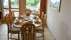 Un coin repas avec une table ronde dressée pour six personnes, entourée de chaises en bois.