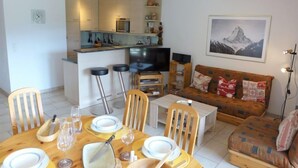 Un salon moderne avec un coin repas, un canapé, un téléviseur et une cuisine en arrière-plan.