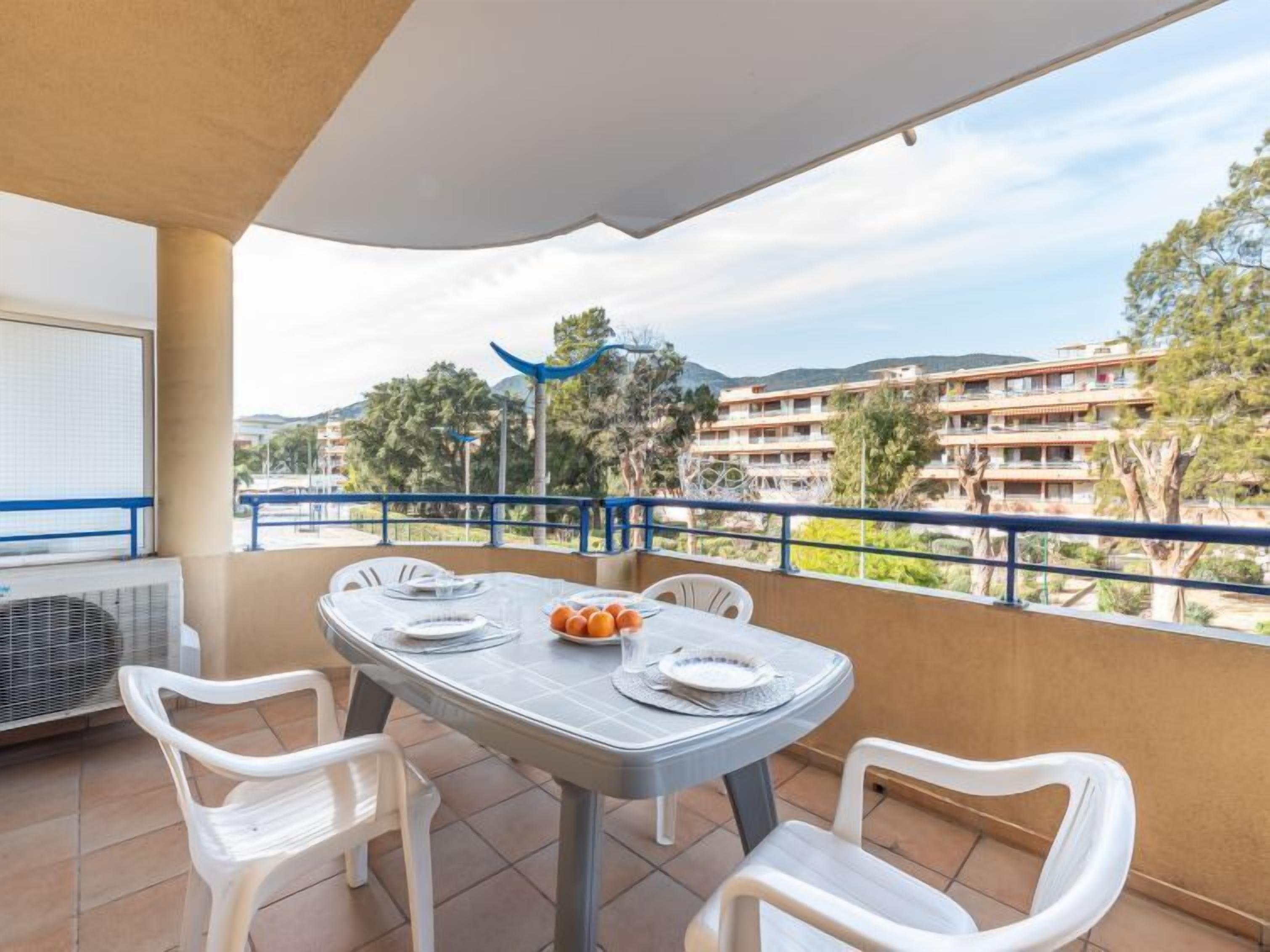 Ein Balkon mit Tisch für zwei Personen, Stühlen und Blick auf ein Wohngebiet mit Gebäuden und Bäumen.