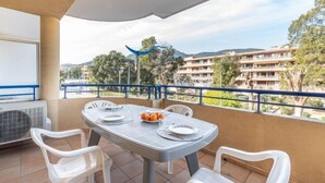 A balcony with a table set for two, chairs, and a view of a residential area with buildings and trees. - Ancre Bleue by Interhome (Cavalaire)