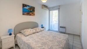 A bedroom with a bed, nightstands, a lamp, a painting, and a window. - Ancre Bleue by Interhome (Cavalaire)