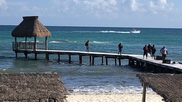 Un muelle que se adentra en el océano con una estructura de techo de paja a la izquierda.