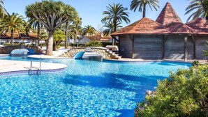 A swimming pool with a stone bridge, palm trees, and a building with a red roof. - El Palmar by Interhome (Dénia)