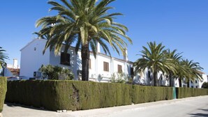 A white building with a tiled roof, surrounded by neatly trimmed hedges and palm trees. - El Palmar by Interhome (Dénia)