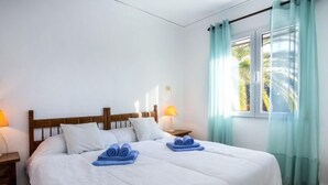 A neatly made bed with white linens and two rolled towels, a wooden headboard, two bedside lamps, and a window with light blue curtains. - El Palmar by Interhome (Dénia)