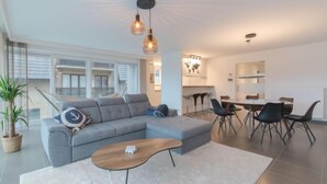 A modern living room with a grey sectional sofa, a wooden coffee table, and a dining area with a round table and black chairs. - Ocean with parking by Interhome (Bredene)