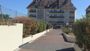 A multi-story building with a central entrance, surrounded by greenery and a paved walkway. - Les Normandières by Interhome (Cabourg)