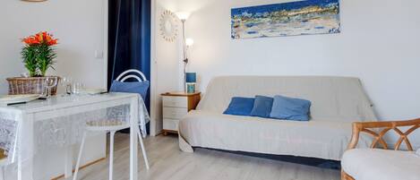 A room with a bed, a dining table with chairs, a lamp, and a painting on the wall.