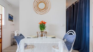 Un'area da pranzo con un tavolo bianco, due sedie, un vaso di fiori e un'opera d'arte a parete.
