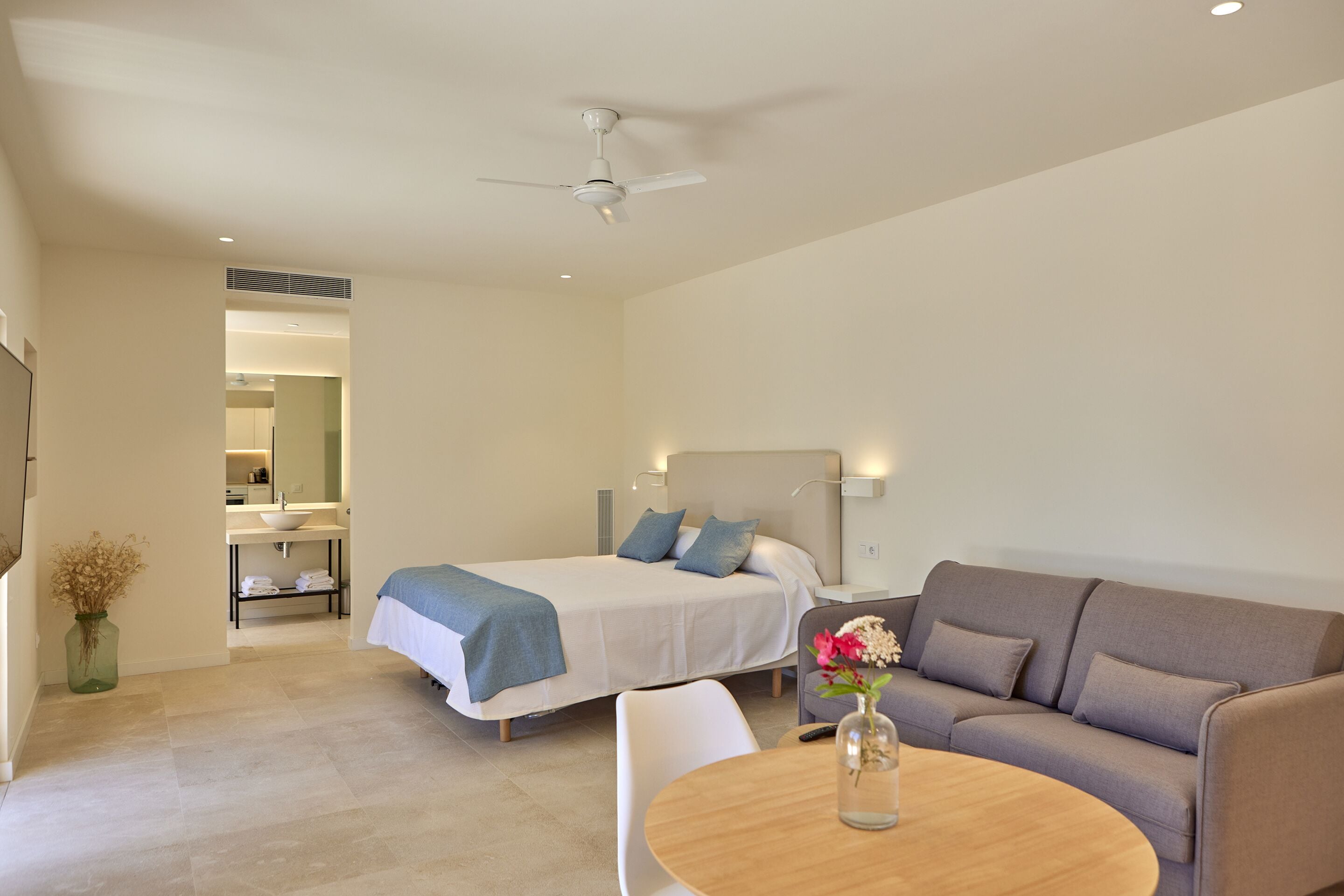 A modern hotel room with a bed, a sofa, a round table, and a ceiling fan.