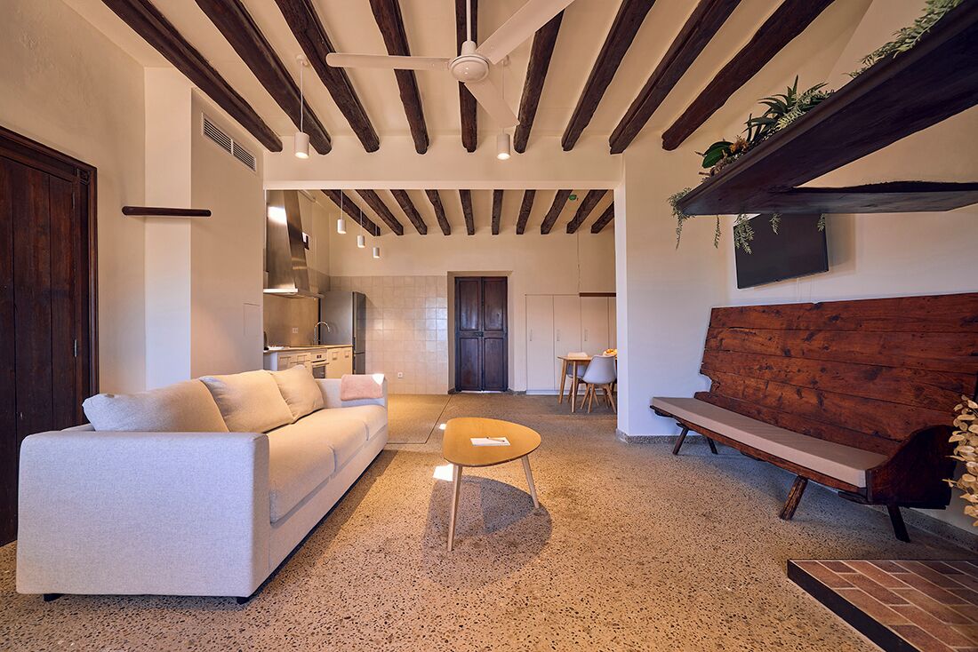 Una sala de estar moderna con un sofá, una mesa de centro, un banco de madera y una cocina al fondo.