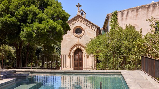 Une piscine bordée d’un mur en pierre et une église dotée d’un clocher.