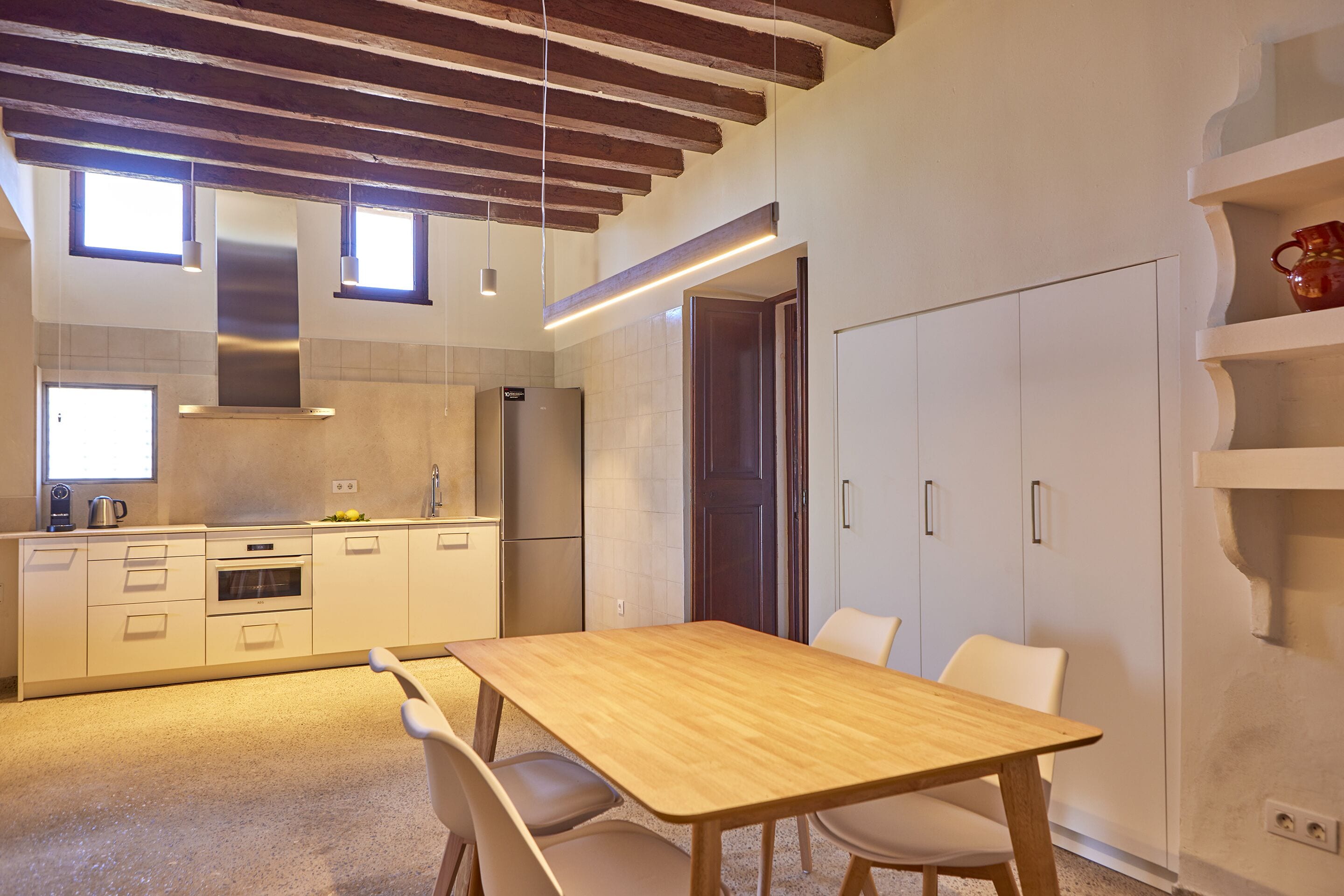 A modern kitchen with white cabinetry, a wooden dining table, and a built-in oven.