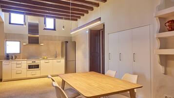 A modern kitchen with white cabinetry, a wooden dining table, and a built-in oven.
