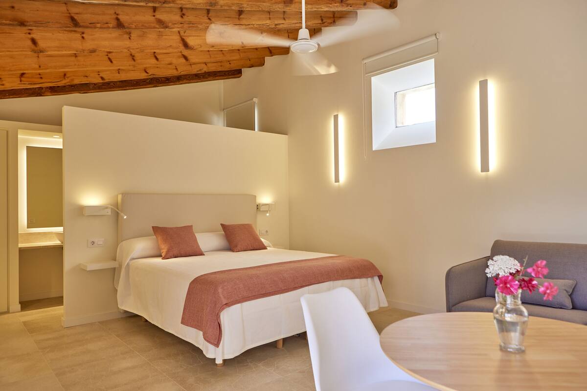 A modern hotel room with a bed, a ceiling fan, a sofa, and a table with a vase of flowers.