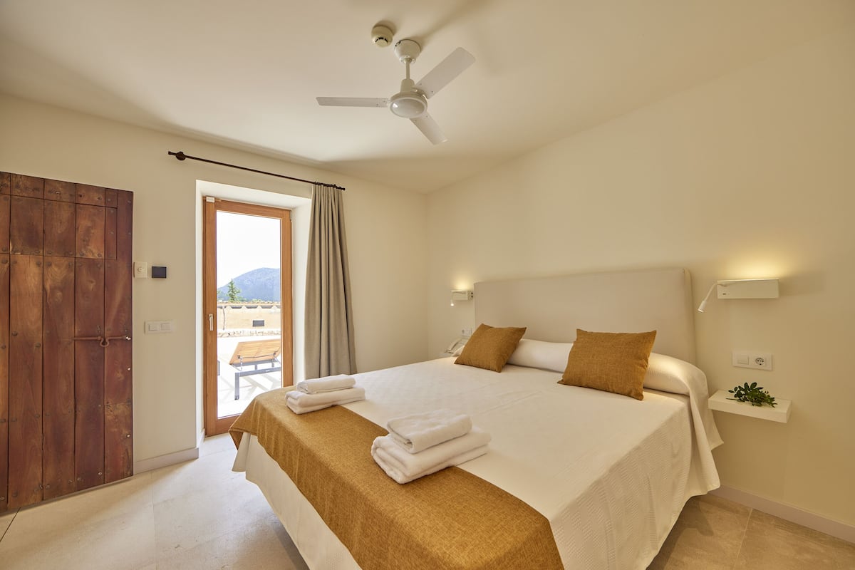 A bedroom with a bed, a ceiling fan, a window with curtains, and a view of the outdoors.