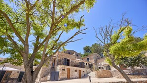 Un bâtiment en pierre avec un escalier menant à un balcon, entouré d’arbres et d’un mur de pierre.